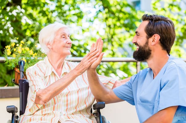 Smiling elderly woman and caregiver engaging in a playful high-five.