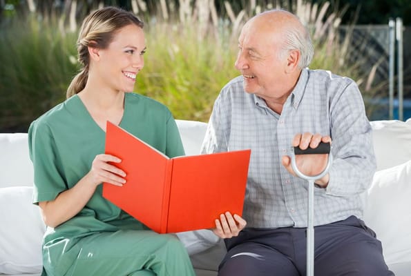 A happy senior resident sits with a caretaker, discussing a red folder outdoors.