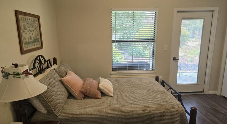 A cozy bedroom with a bed, decorative pillows, and a view of the outdoors through a window.