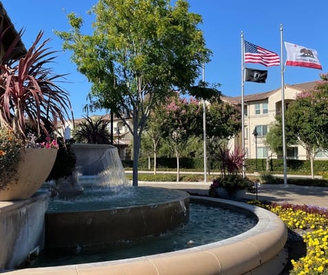 A decorative fountain surrounded by flowers and flags at a senior living facility