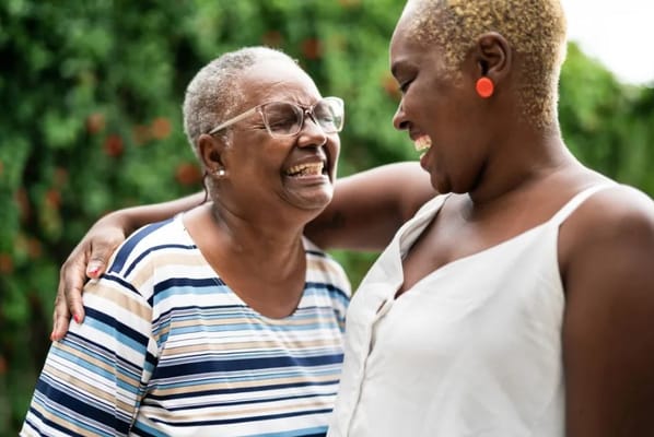 Two smiling women sharing a warm embrace outdoors.
