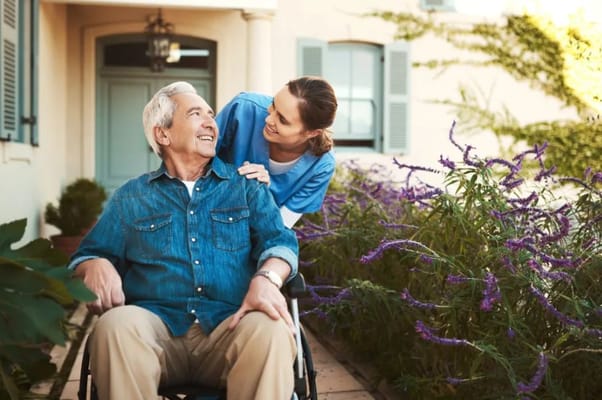 Senior man in a wheelchair smiling with caregiver in a garden