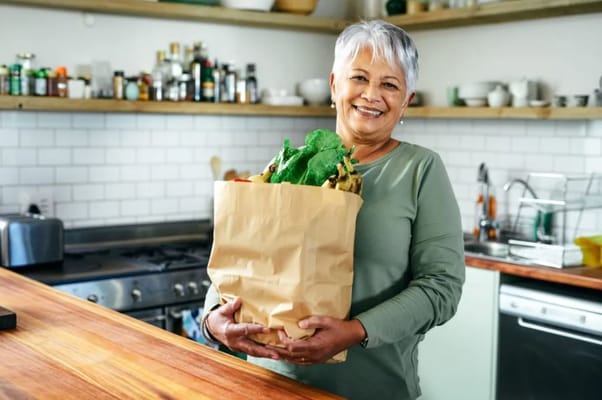 Smiling senior woman holding a paper bag filled with groceries in a kitchen