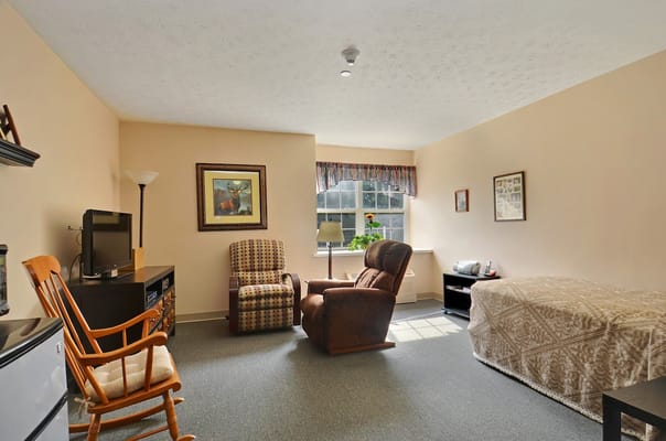 A cozy bedroom with a recliner, armchair, and a window.