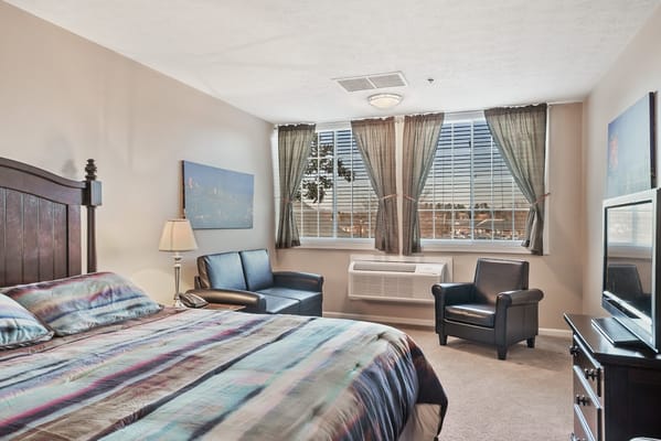 Well-furnished bedroom with a bed, seating area, and large window