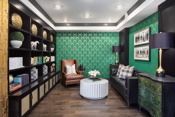 A cozy lounge with a green patterned wall, bookshelves, and comfortable seating.