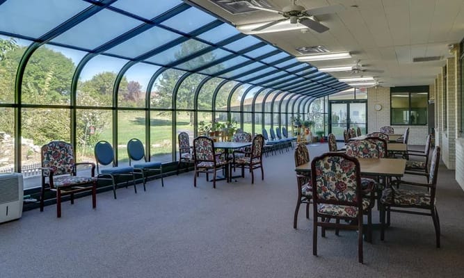 Bright sunroom with tables and chairs surrounded by large windows.