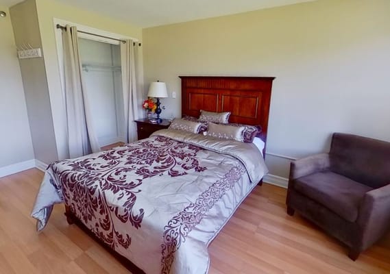 Well-furnished bedroom with a bed, chair, and lamp.