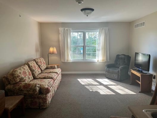 Spacious living room with floral couch, armchair, and TV.