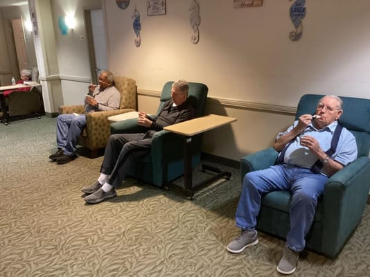 Three senior men sitting in comfortable chairs in a lounge area, enjoying snacks