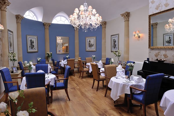 A beautifully set dining room with blue walls, elegant chairs, and a chandelier.