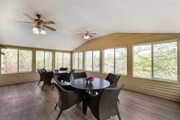 Bright sunroom with tables and chairs overlooking greenery.