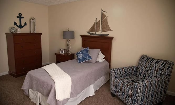 Interior view of a cozy bedroom with a bed, dresser, and armchair.