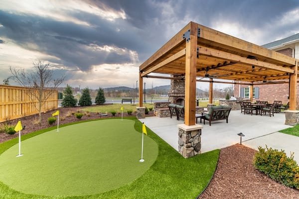 Artificial grass golf putting area with seating under a wooden pergola.