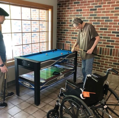 Two residents playing pool at a table in a common area.