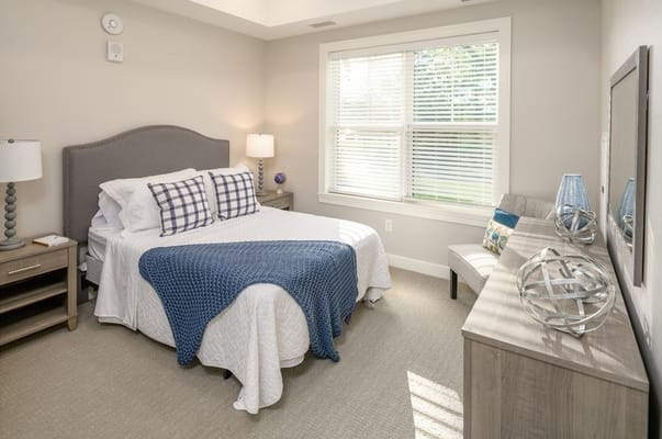 A well-decorated bedroom with a bed, nightstand, and large window.