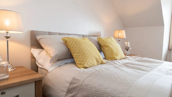 A cozy bedroom featuring a bed with yellow patterned pillows and bedside lamps.
