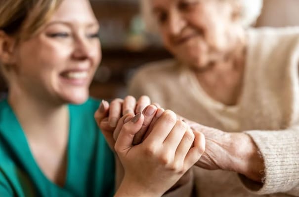 A caregiver and a senior resident holding hands in a warm setting.
