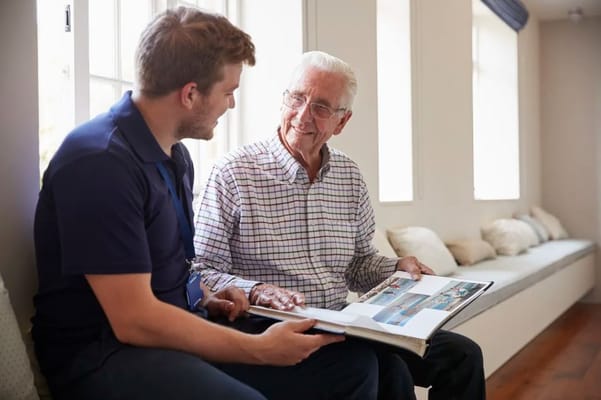 Senior man smiling while looking at a photo album with a staff member