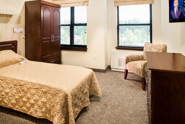 Cozy bedroom in assisted living facility with a bed, dresser, and chair.