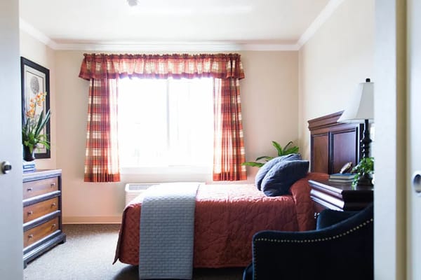 Comfortable bedroom with a window, quilted bedspread, and dresser.