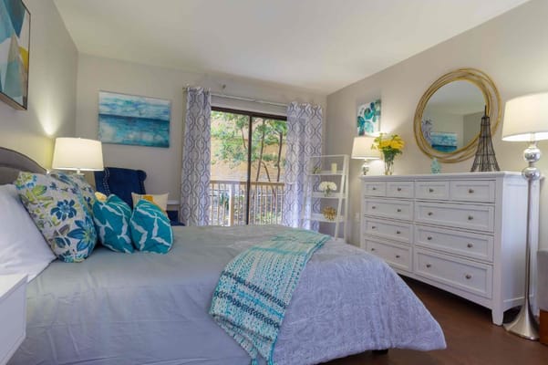 Bright bedroom with a large bed, decorative pillows, and a view of greenery outside.