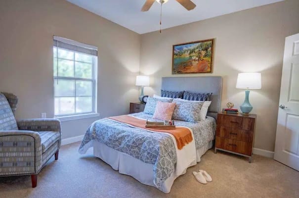 A well-decorated bedroom featuring a bed, decorative pillows, a chair, and nightstands with lamps.