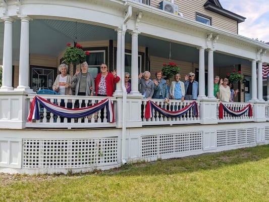 Group of seniors waving from the porch with flower baskets.