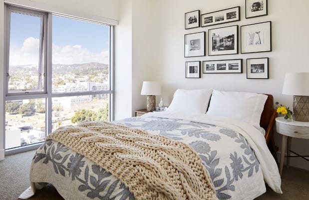 Stylish bedroom featuring a large window with a view, cozy bedding, and decorative artwork.
