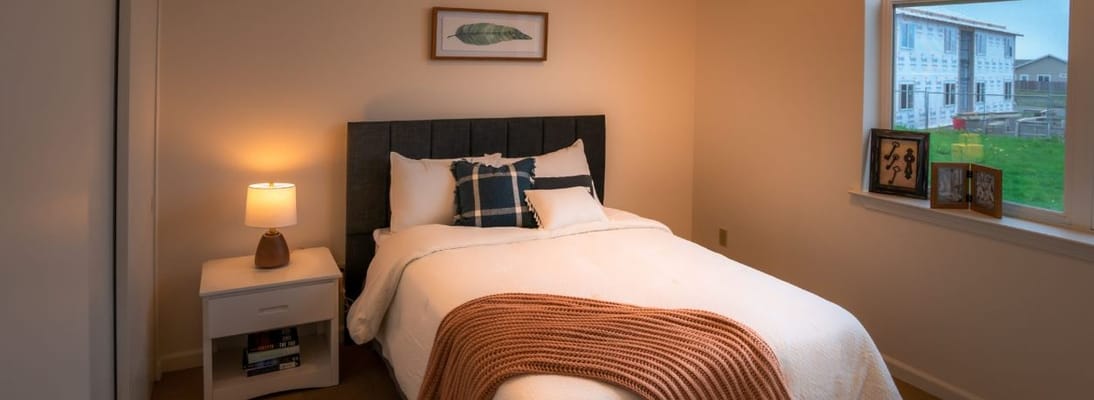 A cozy bedroom with a bed, bedside lamp, and window view.