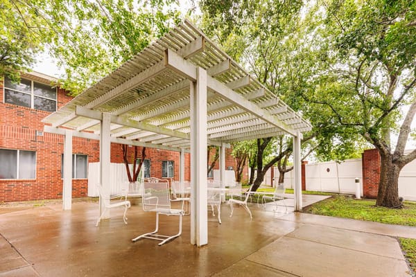 Covered outdoor seating area with white chairs and greenery