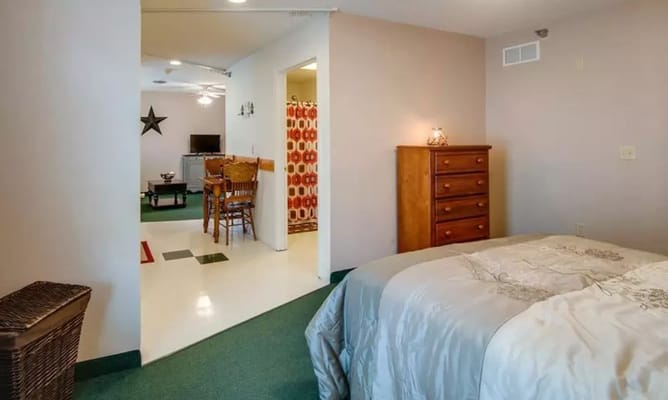 A bedroom with an adjoining living area featuring a dining table and a television.