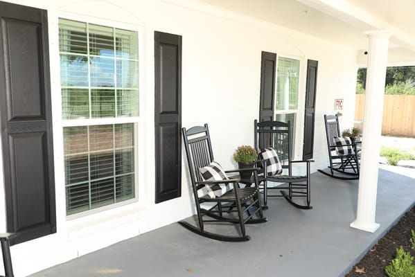 Two black rocking chairs on a porch with white walls and windows