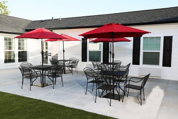 Outdoor patio with red umbrellas and black tables at Victorious Assisted Living