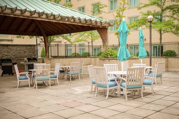 Outdoor seating area with tables and chairs under a gazebo with blue umbrellas.