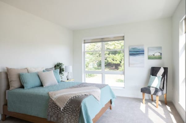 Brightly lit bedroom with a bed, chair, and window view.