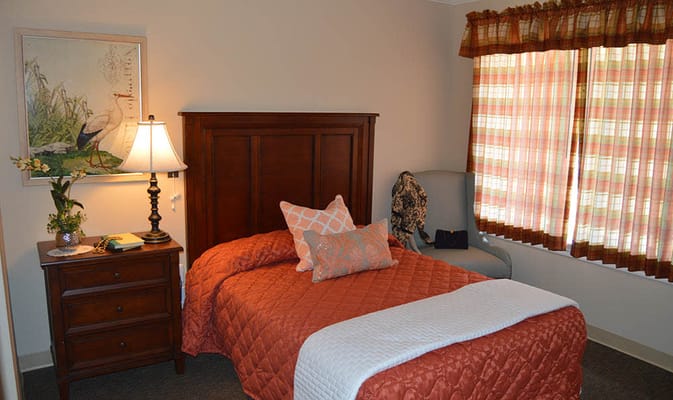 A well-decorated resident room with a bed, lamp, and window curtains.