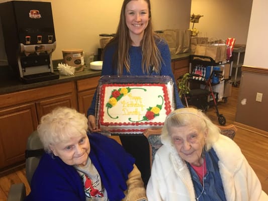 A staff member holding a birthday cake with two residents smiling.