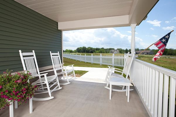 White rocking chairs on a porch overlooking a landscape with a flag
