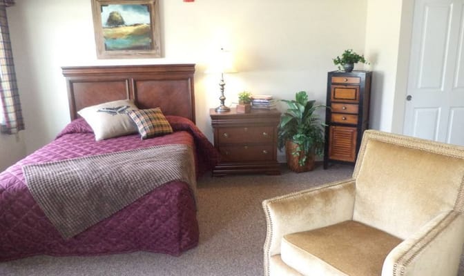 A cozy bedroom with a bed, nightstand, lamp, and armchair.