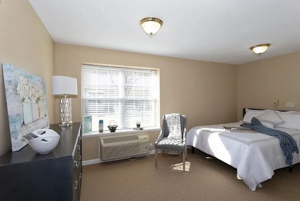 Brightly lit bedroom with a bed, chair, and window.