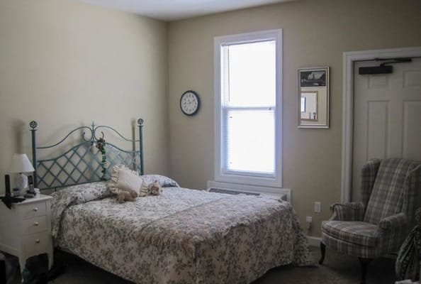 A comfortable bedroom with a floral bedspread, a green metal bed frame, and a cozy armchair.