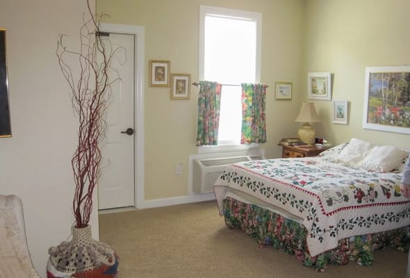 A cozy bedroom featuring a floral bedspread, a lamp, and curtains with vibrant patterns.