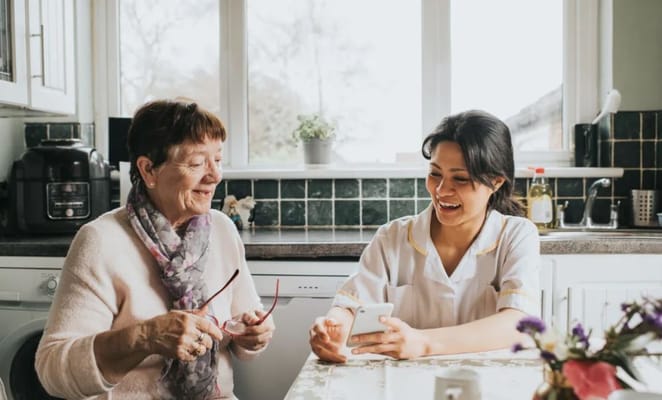 A senior woman and a caregiver sharing a light moment in a kitchen