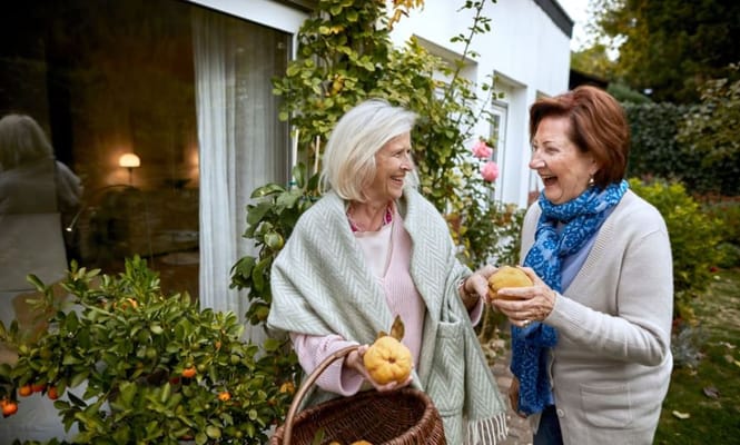Two women laughing and holding fruit in a garden setting