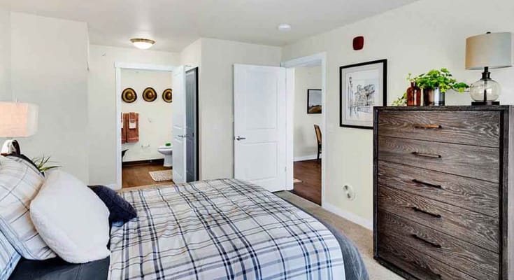 A neatly arranged bedroom with a bed, dresser, and adjoining bathroom