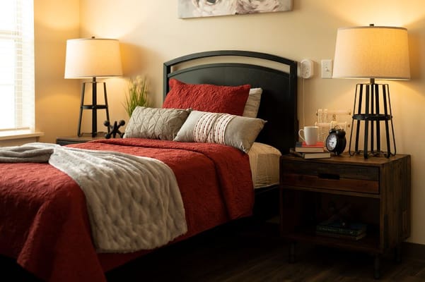 A cozy bedroom with a red quilt, decorative pillows, and bedside lamps.