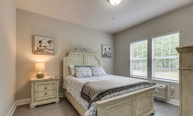 A well-furnished bedroom with a bed, nightstand, and windows.
