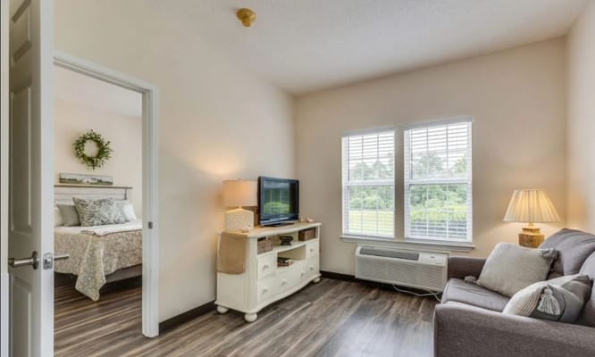 A cozy living room with a TV, couch, and windows in a senior living facility.