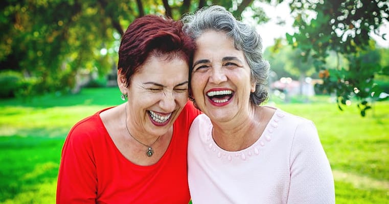 Two senior women laughing together in a garden
